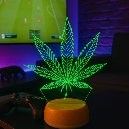 Glowing cannabis leaf lamp on a table with a TV displaying a sports game in the background.